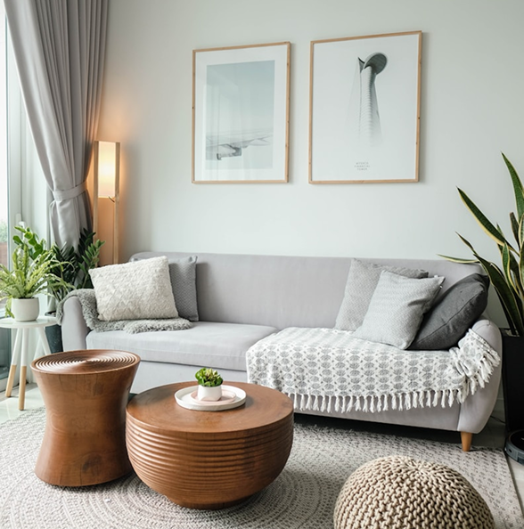 Cozy and modern living room with a light gray sofa, wooden coffee tables, indoor plants, and framed wall art.