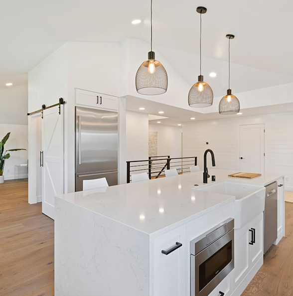 Modern white kitchen interior with pendant lighting, island countertop, and stainless steel appliances.